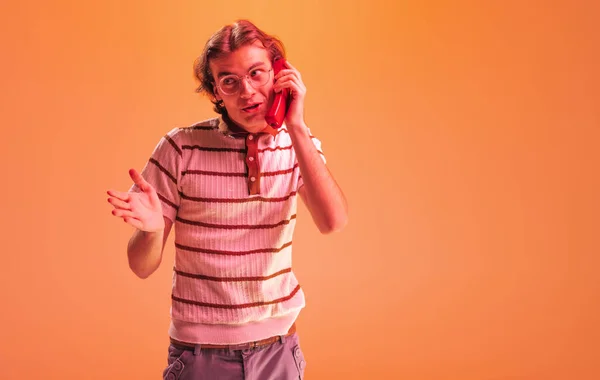 Portret Emocjonalnego Młodzieńca Rozmawiającego Przez Retro Telefon Pozującego Pomarańczowym Tle — Zdjęcie stockowe