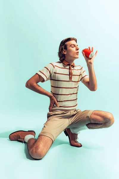 Portrait of young man in retro style outfit, drinking coke, posing isolated over light blue studio background. Concept of youth, fashion, lifestyle, emotions. Copy space for ad