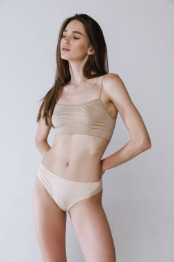 Gri stüdyo arka planında izole edilmiş bej iç çamaşırlı kahverengi düz saçlı genç bir kadının portresi. Güzellik, vücut ve cilt bakımı, sağlık, spa, diyet, spor, kozmetik, reklam