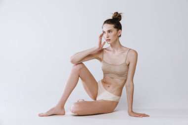 Gri stüdyo arka planında izole edilmiş rahat pamuklu iç çamaşırlarıyla poz veren ince vücutlu genç kızın portresi. Güzellik, vücut ve cilt bakımı, spor, sağlık, kaplıca, kozmetik, reklam