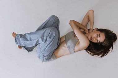 Gri arka planda izole edilmiş kot pantolon ve pamuklu iç çamaşırlarıyla yerde yatan güzel bir kızın portresi. Sağlıklılık. Güzellik, vücut ve cilt bakımı, sağlık, kaplıca, kozmetik, reklam