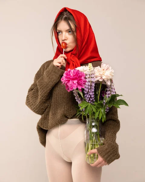 身穿红头巾 毛衣和白色紧身衣的少女的画像 与花朵和棒棒糖在灰色的背景上隔离 复古时尚 艺术摄影 美的概念 — 图库照片