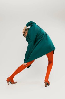 Gri stüdyo arka planında izole edilmiş yeşil ceketli ve parlak turuncu taytlı şık bir kızın arka plan portresi. Eski moda kavramı, sanat fotoğrafçılığı, stil, nonoş, güzellik.