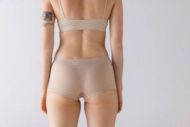 Kırpılmış kadın vücudu, gri stüdyo arka planında izole edilmiş bej iç çamaşırlı arka kalçalar. Tıbbi bakım. Güzellik, vücut ve cilt bakımı, sağlık, estetik cerrahi, kozmetik, reklam
