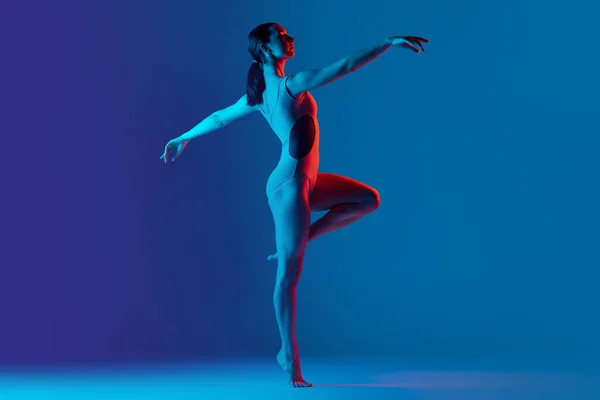 stock image Portrait of young sportive girl doing stretching exercises isolated over blue studio background in neon light. Dancing moves. Concept of sport, strength, health, hobby, youth, lifestyle, ad