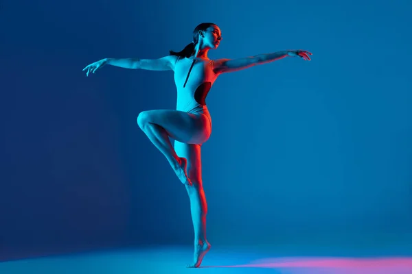 ネオンの光の中で青のスタジオの背景に隔離されたストレッチ練習 トレーニング ダンスを行う若いスポーツ少女の肖像画 スポーツ ライフスタイル 広告の概念 — ストック写真