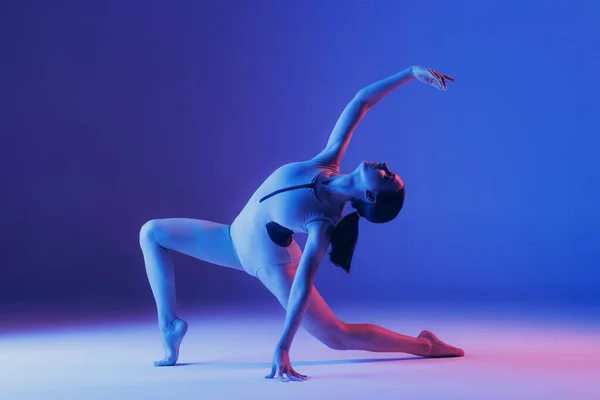 ネオンの光の中で青のスタジオの背景に隔離されたストレッチ演習を行う若いスポーツ少女の肖像画 柔軟性 スポーツ ライフスタイル 広告の概念 — ストック写真