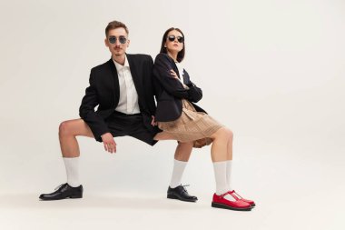 Gri stüdyo arka planında izole edilmiş, retro takım elbiseli şık bir kadın ve erkeğin tam boy portresi. Dizlerinin üzerinde oturuyor. Eski moda kavramı, sanat fotoğrafçılığı, stil, nonoş, güzellik.