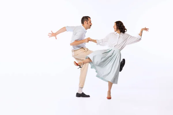Portrait of young cheerful couple, man and woman, dancing boogie woogie isolated over white studio background. Concept of vintage fashion, hobby, activity, art, music, party, creativity and ad