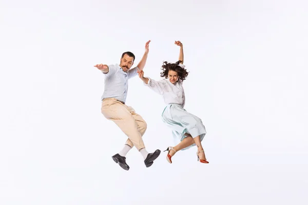 Portrait of young beautiful couple, man and woman, dancing, jumping isolated over white studio background. Concept of vintage fashion, hobby, activity, art, music, party, creativity and ad