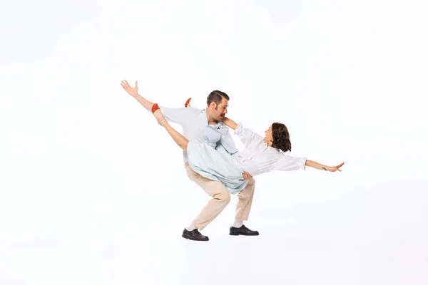 Portrait of young beautiful couple, man and woman, dancing twist isolated over white studio background. Concept of vintage fashion, hobby, activity, art, music, party, creativity and ad