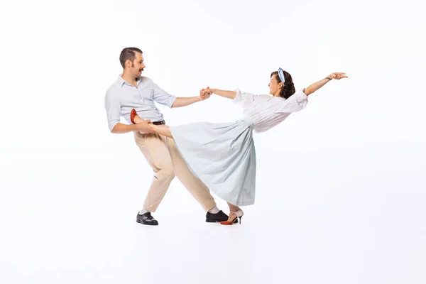 Portrait of young beautiful couple, man and woman, dancing rock and roll isolated over white studio background. Concept of vintage fashion, hobby, activity, art, music, party, creativity and ad
