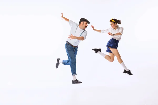Portrait of excited, cheerful couple, man and woman, dancing, having fun isolated over white studio background. Concept of vintage fashion, hobby, activity, art, music, party, creativity and ad