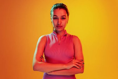 Güzel bir genç kızın portresi, dikkatlice kameraya bakıyor sarı arka planda neon ışıkta izole edilmiş. Duyguların kavramı, yüz ifadesi, yaşam tarzı, moda, gençlik kültürü