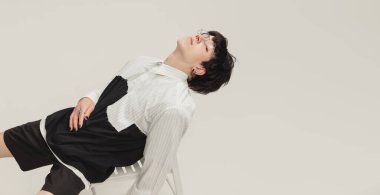 Gri stüdyo arka planında izole edilmiş sakin ve rahatlatıcı görünümlü sandalyede oturan şık genç bir çocuğun portresi. Modern moda kavramı, sanat fotoğrafçılığı, stil, nonoşluk, eşsizlik, reklam