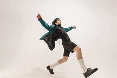 Gri stüdyo arka planında izole bir şekilde poz veren şık giyinmiş genç bir adamın portresi. Özgür hissediyorum. Modern moda kavramı, sanat fotoğrafçılığı, stil, nonoşluk, eşsizlik, reklam