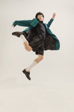 Gri stüdyo arka planında izole edilmiş siyah elbiseli ve yeşil ceketli şık bir gencin portresi. Çok hoş görünüyor. Modern moda kavramı, sanat fotoğrafçılığı, stil, nonoşluk, eşsizlik, reklam