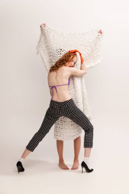 Gri arka planda, örülmüş ekoseyle kaplı gizli kişiye sarılan zarif genç bir kadının portresi. Gizli tutku. Retro moda, sanat fotoğrafçılığı, stil, nonoş, güzellik, gençlik kavramı