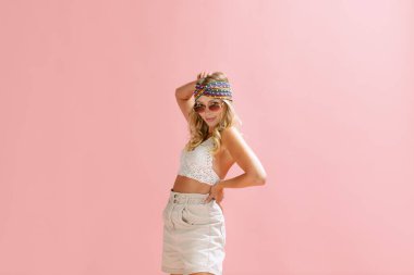 Pembe stüdyo arka planında izole bir şekilde poz veren zarif genç kadın portresi. Yaz festivali kıyafeti. Güzellik kavramı, duygular, yüz ifadesi, yaşam tarzı, moda, gençlik kültürü