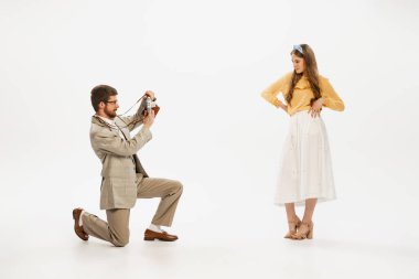 Beyaz arka planda izole edilmiş retro kameralı güzel genç kadınların fotoğrafını çeken genç bir adamın portresi. Eski moda, tarz, gençlik kültürü, duygular, güzellik kavramı. İlan için alanı kopyala