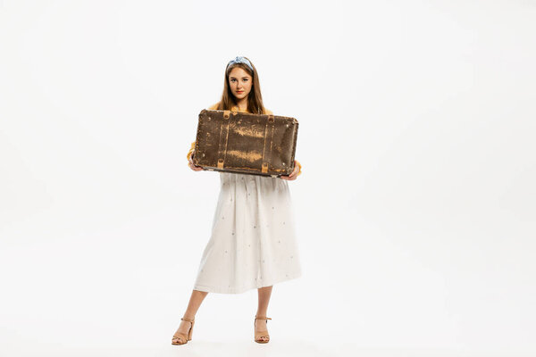 Portrait of stylish, beautiful, young woman posing with vintage suitcase isolated over white studio background. Concept of retro fashion, style, youth culture, emotions, beauty, ad
