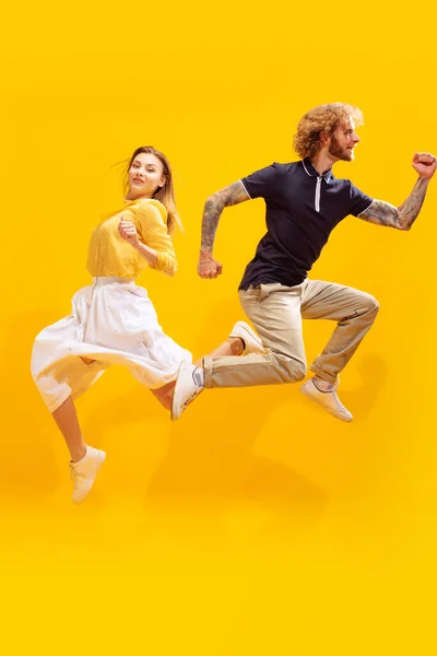 Portrait of young man and woman in casual clothes posing isolated over yellow studio background. Jumping in excitement. Concept of youth, lifestyle, relationship, emotions, facial expression, ad