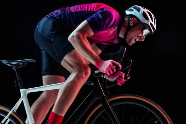 İnsan portresi, profesyonel bisikletçi eğitimi, neon ışıklarıyla izole edilmiş siyah stüdyo arka planında at sürmek. Hız. Spor, eylem, hareket, hız, hobi, yaşam tarzı kavramı. İlan için alanı kopyala