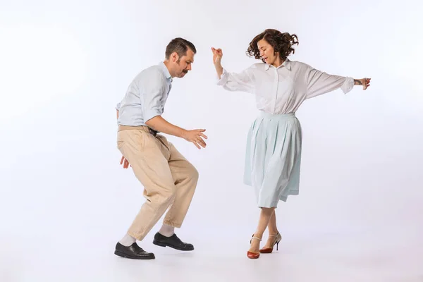 Portrait of young attractive couple, man and woman, dancing isolated over white studio background. Cheerful lifestyle. Concept of vintage fashion, hobby, activity, art, music, party, creativity and ad