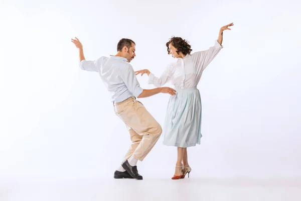 Portrait of young beautiful couple, man and woman, dancing isolated over white studio background. Ecstatic dance. Concept of vintage fashion, hobby, activity, art, music, party, creativity and ad