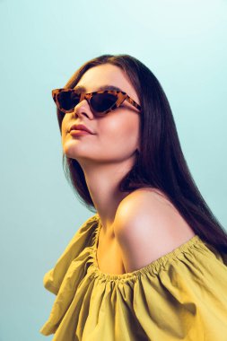 Yeşil stüdyo arka planında izole edilmiş şık elbiseli ve moda güneş gözlüklü genç kız portresi. Gençlik kavramı, moda, yaşam tarzı, duygular, yüz ifadesi. İlan için alanı kopyala