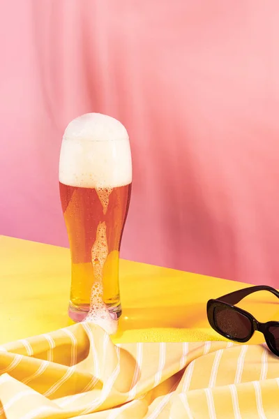 Glass of chill foamy lager beer isolated over pink yellow background. Summer pool party. Vacation. Concept of cocktails, alcoholic drinks, taste, party, mix. Copy space for ad. Retro style