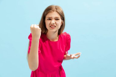 Mavi stüdyo arka planında, yumruklarıyla poz veren duygusal genç kız portresi. Sinir bozucu. Güzellik anlayışı, tarz, yaşam tarzı, gençlik, duygular, yüz ifadesi. İlan için alanı kopyala