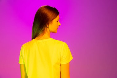 Pembe arka planda neon ışıkta izole edilmiş beyaz tişörtle poz veren genç kız portresi. Arkadan bak. Güzellik anlayışı, tarz, yaşam tarzı, gençlik, duygular, yüz ifadesi. İlan için alanı kopyala