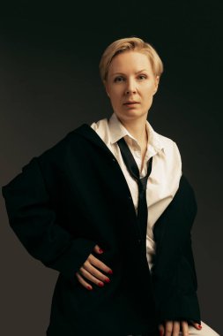 Güzel orta yaşlı kadın portresi, şık siyah erkek tarzı takım elbiseli, koyu arka planda izole edilmiş poz veriyor. Ciddi bir bakış. Güzellik kavramı, moda, tarz, canlı portre. İlan için alanı kopyala