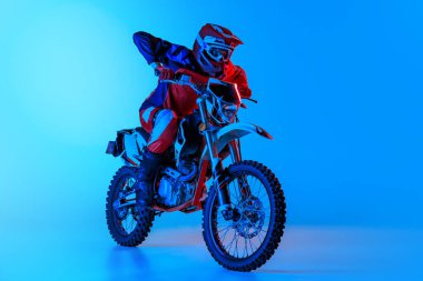 Genç bir adamın portresi, motosiklet kullanan tam teçhizatlı bir motosikletçi mavi bir arka planda, neon ışıkta izole edilmiş. Motosport, hız, aksiyon, hobi, rekabet kavramı. İlan için alanı kopyala