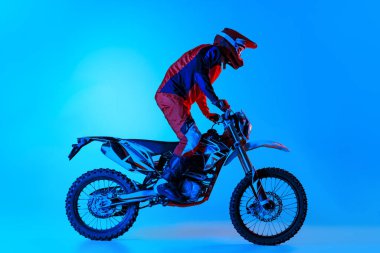 Motosikletli genç bir adamın portresi, mavi renkli arka planda neon ışıklarıyla izole bir şekilde bisiklete biniyor. Motosport, hız, aksiyon, hobi, rekabet kavramı. İlan için alanı kopyala