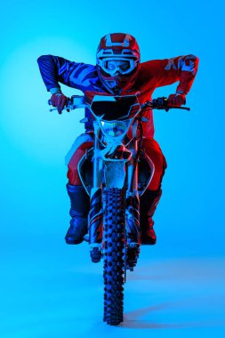 Motosiklet süratini geliştiren konsantre genç bir adamın portresi neon ışıklarıyla izole edilmiş mavi stüdyoda izole edilmiş. Motosport, hız, aksiyon, hobi, rekabet kavramı. İlan için alanı kopyala