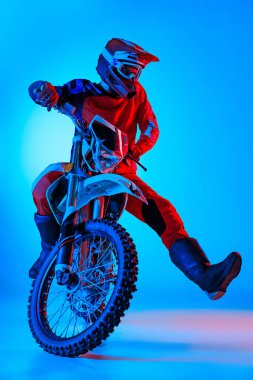 Motosikletli bir motorcunun portresi mavi stüdyo arka planında neon ışıkta izole edilmiş. Hızla dönüyor. Motosport, hız, aksiyon, hobi, rekabet kavramı. İlan için alanı kopyala