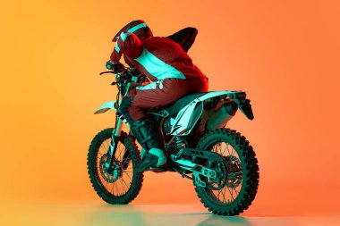 Genç bir adamın portresi, motosiklet kullanan tam teçhizatlı bir motosikletçi turuncu stüdyo arka planında neon ışıklarıyla izole edilmiş. Büyüme hızı. Motosport, aksiyon, hobi, rekabet kavramı. İlan için alanı kopyala