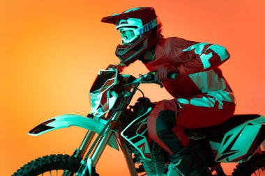 Genç bir adamın portresi, motosiklet kullanan tam teçhizatlı bir motosikletçi turuncu stüdyo arka planında neon ışıklarıyla izole edilmiş. Yarış. Motosport, hız, aksiyon, hobi, rekabet kavramı. İlan için alanı kopyala