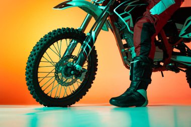 Erkek görüntüsü, çizmeli motosikletli bacağı ve turuncu stüdyo arka planında izole edilmiş motosiklet lastiği. Motosport, hız, aksiyon, hobi, rekabet kavramı. İlan için alanı kopyala