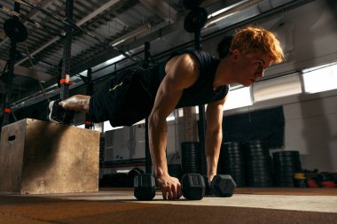 Spor salonunun arka planında izole edilmiş halterlerle şınav çeken genç kaslı kızıl saçlı adamın portresi. Spor, sağlık, eylem, beslenme, gençlik kavramı. İlan için alanı kopyala