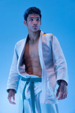 Genç, sportif bir adam mavi stüdyo arka planında neon ışıkta yalnız poz veriyor. Profesyonel karışık dövüş sporcusu. Dövüş sanatı kavramı, dövüş sporu, sağlık, güç, enerji, formda. İlan için alanı kopyala