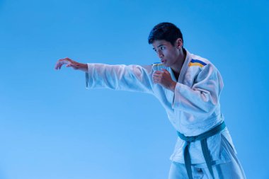 Genç sporcu pozu portresi, neon ışıkta mavi stüdyo arka planında izole edilmiş antrenman yumruk egzersizleri. Dövüş sanatı kavramı, dövüş sporu, sağlık, güç, enerji, formda. İlan için alanı kopyala