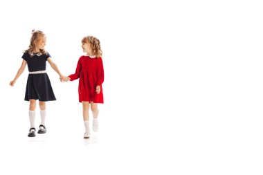 İki küçük kızın portresi, güzel elbiseli çocuklar el ele tutuşmuş, beyaz arka planda mutlu bir şekilde yürüyorlar. Çocukluk kavramı, arkadaşlık, eğlence, yaşam tarzı, moda. Retro biçimi