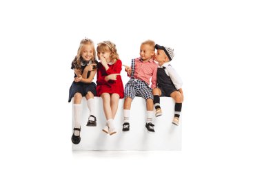 Çocukların portresi, erkeklerin ve kızların birlikte oturması, fısıldaması, kıkırdaması beyaz stüdyo arka planında izole edilmiş. Çocukluk kavramı, arkadaşlık, eğlence, yaşam tarzı, moda. Retro biçimi