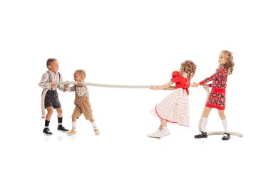 Beyaz stüdyo arka planında izole edilmiş halatı çeken oyuncu çocuklar, oğlanlar ve kızların portresi. Rakipler. Çocukluk kavramı, arkadaşlık, eğlence, yaşam tarzı, moda. Retro biçimi