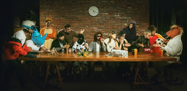 Group of people standing, sitting at the long table in different costumes, indoors and cheering up crying woman in image of widow. Funny, modern replica of last supper painting. Comical life situation
