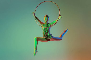 Portrait of young, muscular girl, female rhytmic gymnast training with hoop isolated over multicolored studio background in neon light. Concept of action, motion, sport life, motivation, competition.