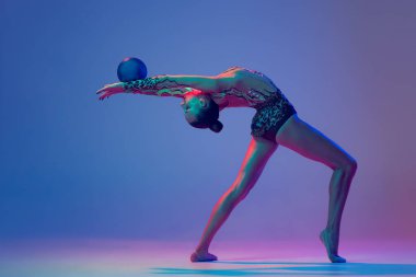 One young girl, rhythmic gymnast athlete performing with blue ball isolated on blue purple background in neon light. Concept of action, motion, sport life, motivation, competition. Copyspace for ad